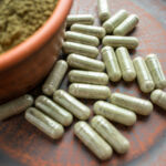 kratom green capsules and powder on brown plate