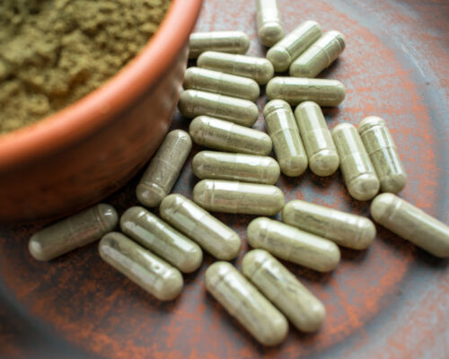 kratom green capsules and powder on brown plate