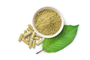 Kratom (Mitragyna speciosa) capsules with powder and green leaf